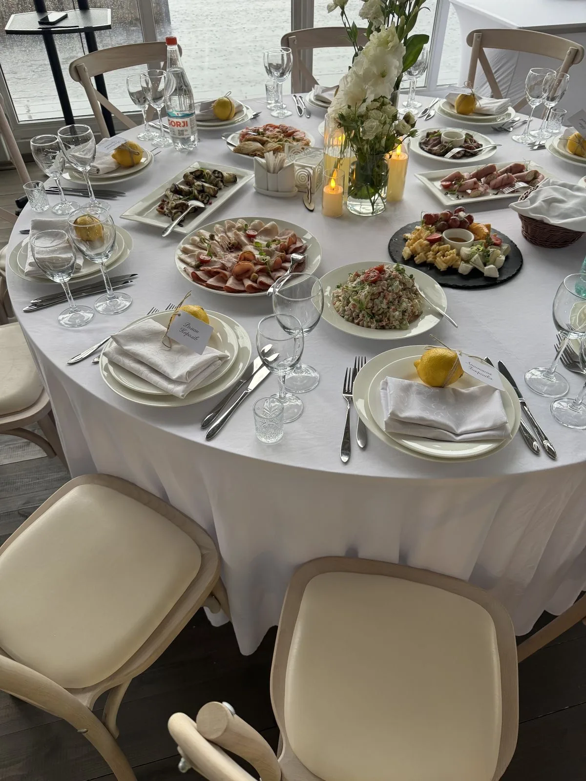 Круглый стол с закусками, лимонами на тарелках и карточками гостей у окна