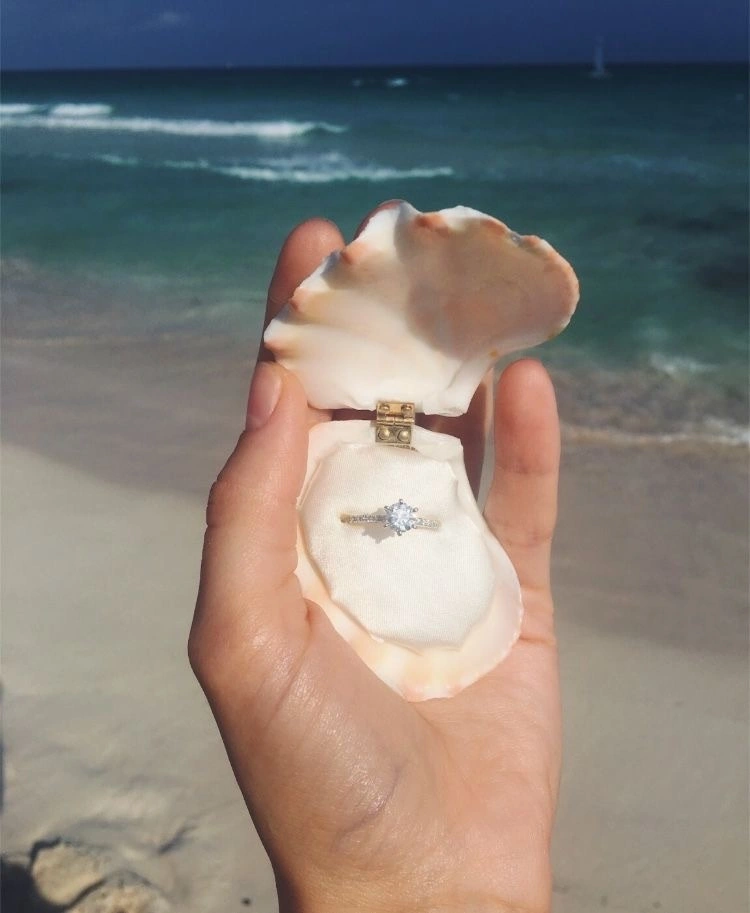 Кольцо в морской ракушке на ладони на фоне моря