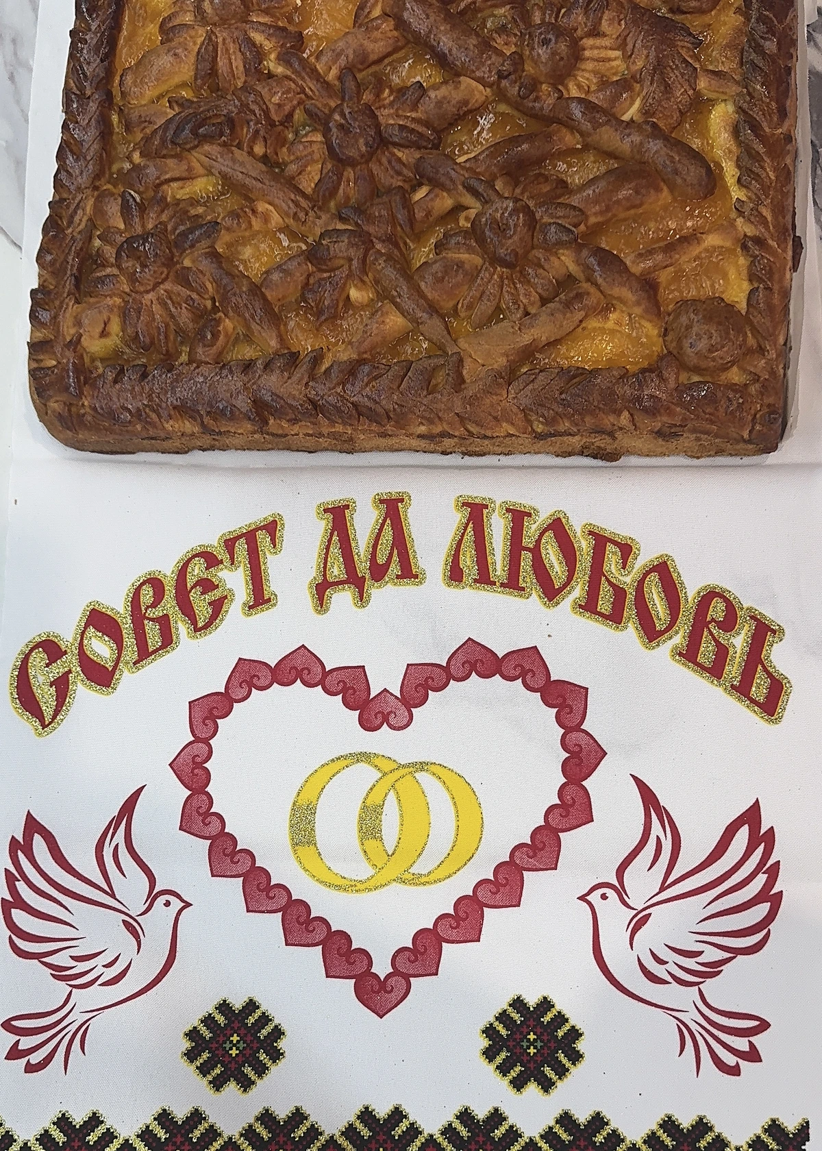 Пирог над рушником с вышитыми голубями, сердцем и обручальными кольцами